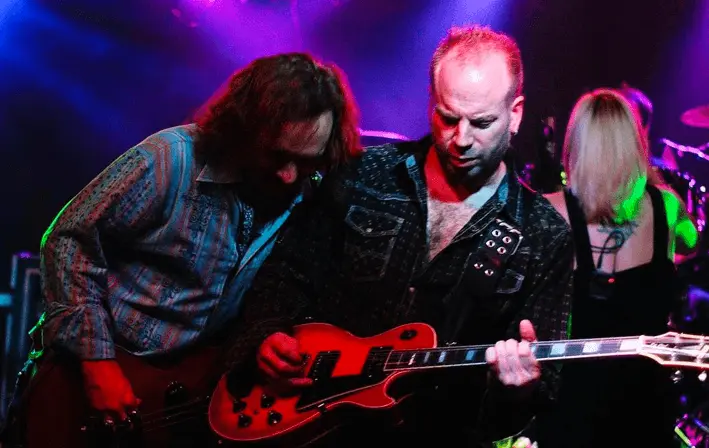 Rock band guitarists performing onstage with red guitar
